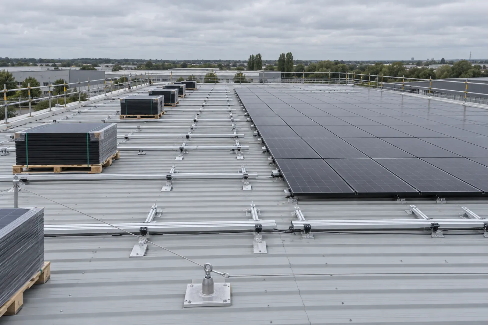 An installation underway on a warehouse roof: modules staged on the deck, mounting rail partly fixed, one section of array complete